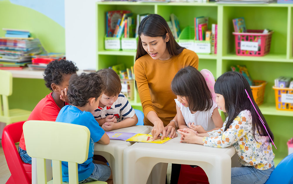 A female teacher reading a book to young children in a classroom.