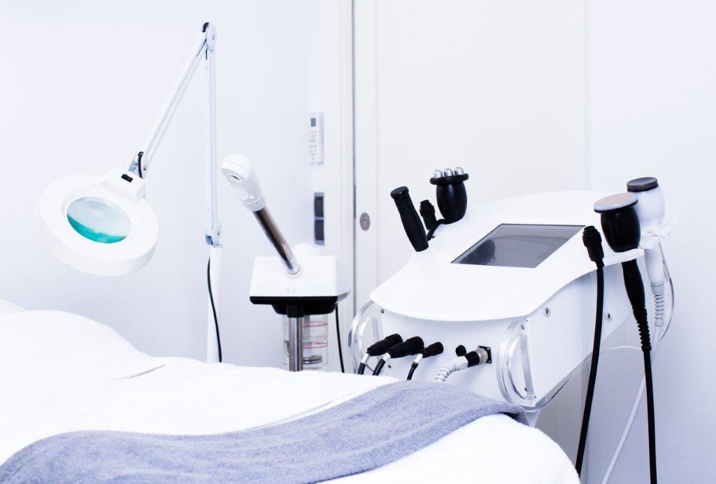 A stock photo showing equipment in a medical spa, including a table, laser machine, and lights.